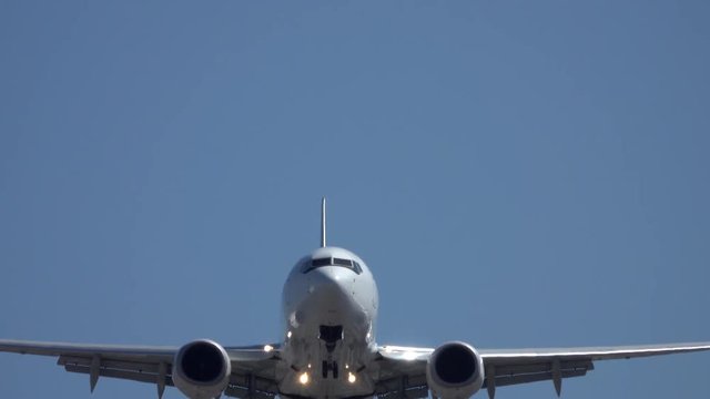 A large, unmarked, commercial jet airliner flies over during final landing approach at an international airport during the day.