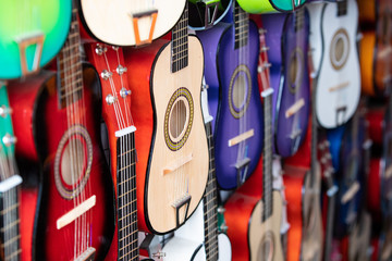 Rows of colorful practice guitars for kids hanging on the wall of a street vendor.