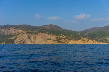 Shoreline with hills covered with vegetation against the blue of sea and sky with clouds