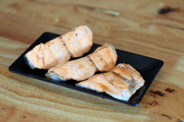 Fototapeta na wymiar Grilled salmon on black dish with dipping soy sauce and green spicy sauce on wooden table