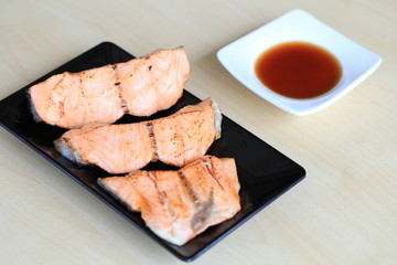Grilled salmon on black dish with dipping soy sauce and green spicy sauce on wooden table