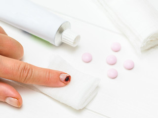A knife-cut index finger of the left female hand, a tube of ointment and a bandage and pills on a...