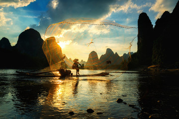 Silhouette of Cormorant fisherman using net on the ancient bamboo boat - obrazy, fototapety, plakaty