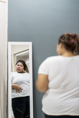 Obese woman looking at her fat belly in the mirror