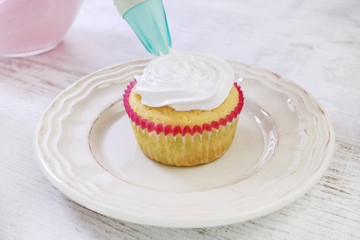Woman prepares muffins decorated with cream and sprinkles.
