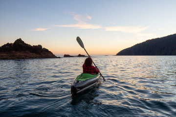 Girl kayaking in the Pacific Ocean during a cloudy summer sunset. Taken in San Josef Bay, Cape Scott, Northern Vancouver Island, BC, Canada.