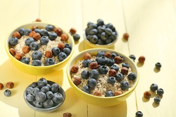 oatmeal porridge with blueberries and hazelnuts. Muesli with berries and nuts.granola and fresh blueberries in a yellow  bowl on a yellow wooden plank background.Useful breakfast.Healthy Eating