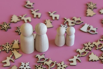family is waiting for the new year. wooden figurines of papa's mom and two children on a pink background with Christmas symbols Christmas tree reindeer snowflakes and a bell