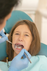 Little girl at the reception in the dentist's office. little girl sitting in a chair near a dentist after dental treatment. Little girl sitts in the dentist's office. vertical photo