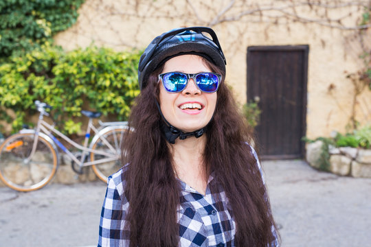 Happy woman with helmet and sunglasses posing backgound bicycle and street