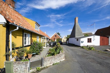 Fototapeta na wymiar Small colorful half-timbered houses in Aarsdale, Bornholm, Denmark. Chimney of traditional smokehouse in the background