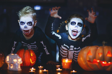 happy Halloween! children in costume of skeletons with pumpkins and candles in dark.