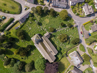 Aerial view above a Church cemetery and houses in an old British village in the countryside. Warm colours give a homely effect.