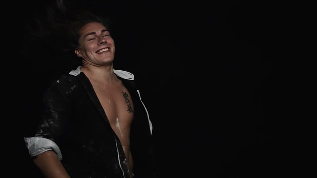 Young cute charismatic brown eyed guy with tattoo on chest, wearing black unbuttoned shirt with short sleeves dramatically turning around and shaking his head demonstrating beautiful long curly hair
