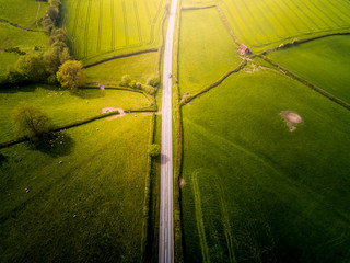 Aerial view looking down on a rural road in the UK countryside with a car racing along it. On a...
