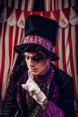 Freaking out magician in magician hat and black outfit shows silence gesture on the scene of the dark circus