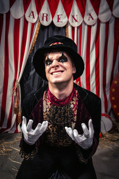 Freaking out magician in magician hat and black outfit shows his dark face on the scene of the dark circus