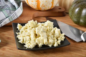 A dish of crumbled organic blue cheese on a cutting board with other ingredients