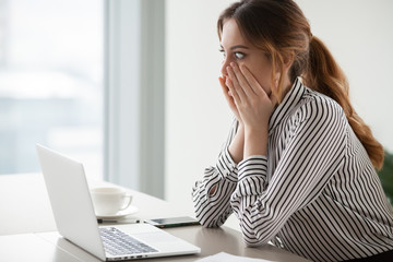 Shocked woman worker looking at laptop screen surprised with bad or unexpected online news, amazed...