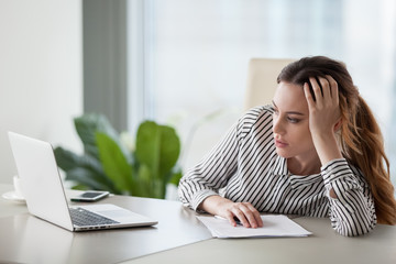 Bored millennial female worker lie at office desk look at laptop screen think about problem...