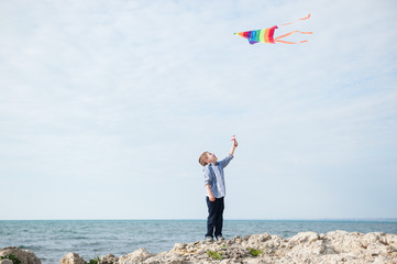 healthy little boy holding flying colorful kite on autumn sea background