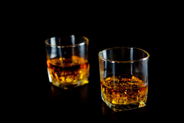 Two glasses of whiskey or whisky with ice on black background.