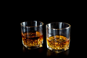 Two glasses of whiskey or whisky with ice on black background.