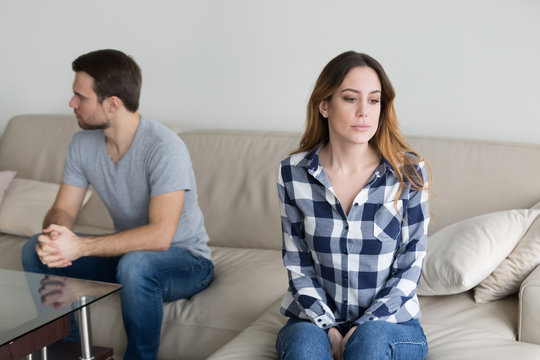 Offended husband and wife sit separately on couch avoid talking or looking at each other, millennial couple in fight ignore spouse, having disagreement or misunderstanding. Family problem concept