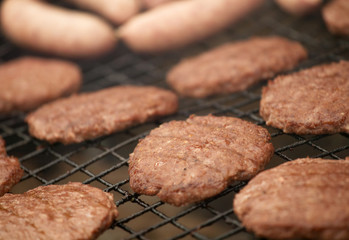 BEEF BURGERS AND SAUSAGES COOKING ON A BARBECUE
