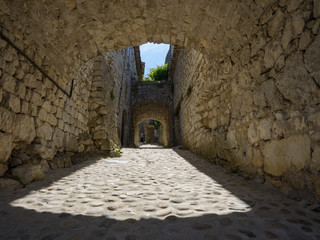 Blick durch alte Mauer auf Pflasterstraße in der Sonne, Frankreich