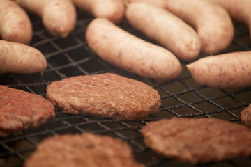 BEEF BURGERS AND SAUSAGES COOKING ON A BARBECUE