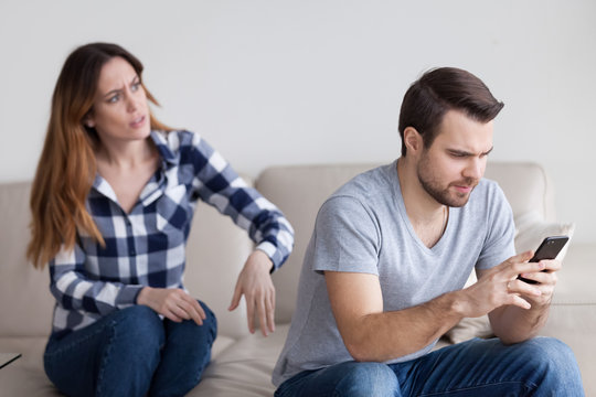 Mad wife shocked by indifferent husband behavior texting to someone, busy with smartphone, suspicious woman argue with beloved man distrusting him. Relationships, cheating problem concept