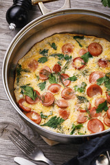 Scrambled eggs with sausage and greens in a frying pan, close-up