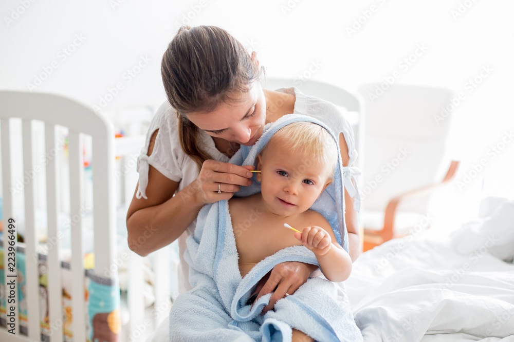 Sticker Mother holding little baby wrapped in towel after bath, cleaning his ears.