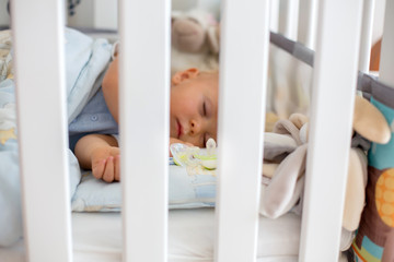 Little baby boy, sleeps in baby bed with pacifier and toys