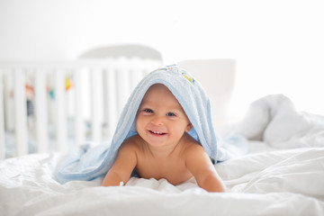 Little cute baby boy, lying in bed with towel after bath, sunny bedroom © Tomsickova