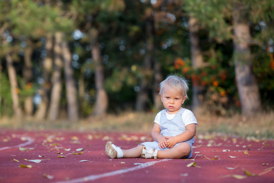 Cute toddler baby boy on a running path on a stadium