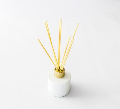Several  sticks standing in a white bottle with a gold-plated lid filled with liquid with a aromatic spicy smell isolated on white background