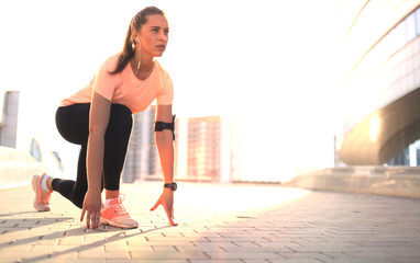 Young fitness attractive sporty girl runner in start position outdoor at sunset or sunrise in city.