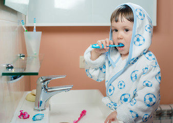 A little girl or child brushes teeth in the bathroom. Hygiene of the oral cavity. Children's toothpaste. the kid is looking at the toothbrush with the paste
