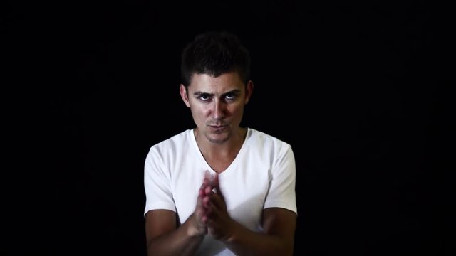 Young handsome sporty male singer with big blue eyes and stylish haircut dressed in white t-shirt is dynamically clapping with hands and looking at camera in studio with black matte background.