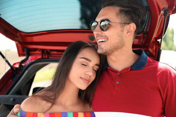 Happy young couple standing near car in shade
