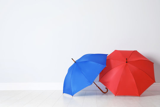 Beautiful open umbrellas on floor near white wall with space for design