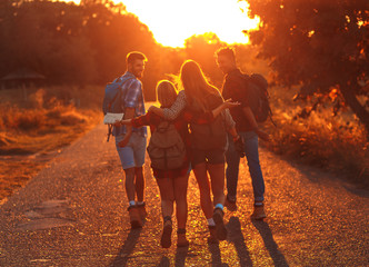 Rear view of group of four friends hiking through countryside together at sunset.