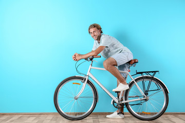 Fototapeta na wymiar Handsome man with bicycle against color wall. Space for text