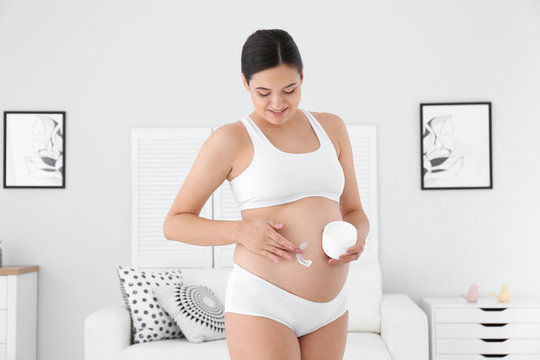 Pregnant woman applying body cream on belly at home