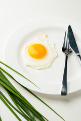 Scrambled eggs on a white plate with a fork and a knife. Green onion near the plate
