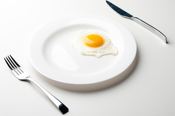 Scrambled eggs on a white plate with a fork and a knife. Green onion near the plate