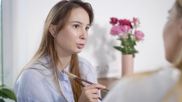 Portrait of attractive brunnete girl talking to a friend in kitchen holding chopsticks, girls time.