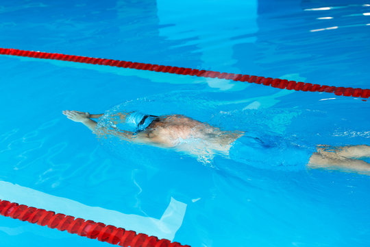 Image top of athletic man in blue cap floating on path in pool
